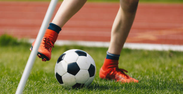 primo primo di young soccer player kicking ball sul campo di calcio. calcio d'angolo calcio in campo. calciatore in tacchette rosse sul prato verde dello stadio - soccer field soccer corner stadium foto e immagini stock