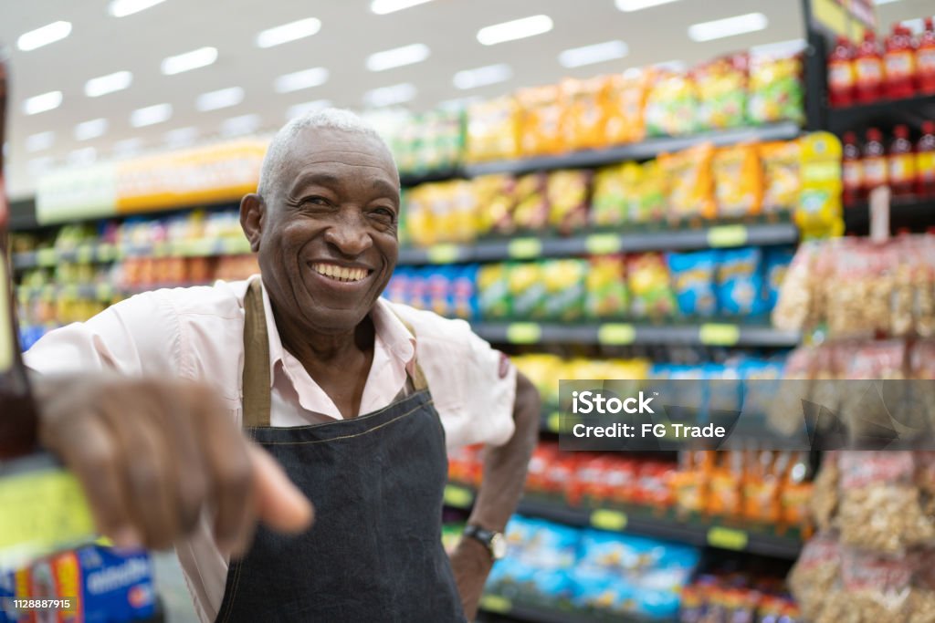 Afro senior man business owner / employee at supermarket Proud to say we're open for business Supermarket Stock Photo