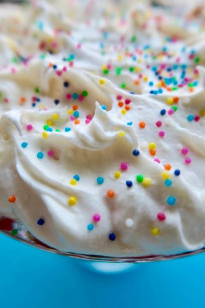 istock Image of whipped cream topping with rainbow multi coloured cake sprinkles / hundreds and thousands, trifle with sponge cake and strawberry jelly 1128890397