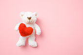 Smiling white teddy bear holding red soft heart on pastel pink background. Mock up for happy, positive idea. Empty place for emotional, sentimental, lovely text, quote or sayings.