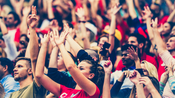 Crowds cheering on a sports stadium Crowd on a stadium cheering with hands up and waving with red balloons. football fans in stadium stock pictures, royalty-free photos & images