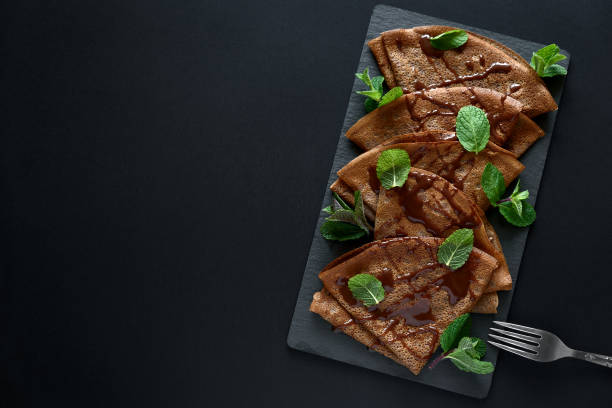 crêpes au chocolat faits maison servis avec les bleuets, sauce et menthe feuilles sur plaque d’ardoise. mise au point sélective. vue de dessus. espace copie - pancake blini russian cuisine french cuisine photos et images de collection