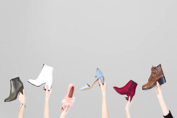 istock Hands holding different woman shoes on grey background. 1128913527