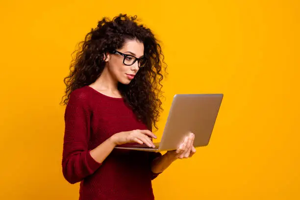 Profile side view portrait of her she nice clever smart intelligent genius cute attractive pretty cheerful wavy-haired lady holding in hands laptop isolated over bright vivid shine orange background