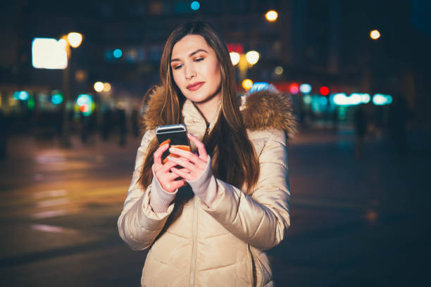 istock Young woman using smart phone on the city at night 1128914453