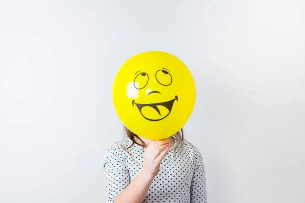 Young pretty girl holding baloon over white background. April fools Day. Smile baloon