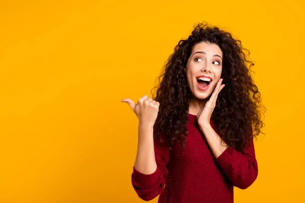 Photo of Close up photo beautiful cheerful amazing her she lady showing way one arm thumb other cheek wondered look empty space wearing red knitted sweater pullover clothes outfit isolated yellow background