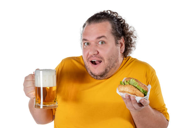istock Funny fat man eating burger and drinking alcohol beverage on white background 1128919819
