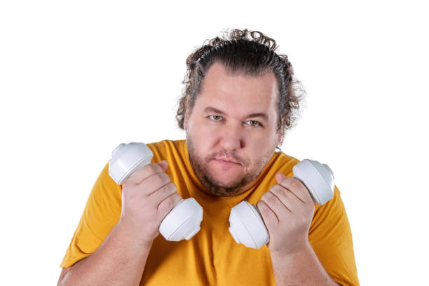 istock Funny fat man exercising with dumbbells and looking at camera isolated on white background 1128919938