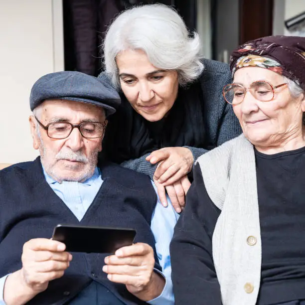 Portrait of senior couple looking at the screen of smartphone together with their senior daughter. The phone is in hands of senior man. Shot indoor with a full frame mirrorless digital camera.