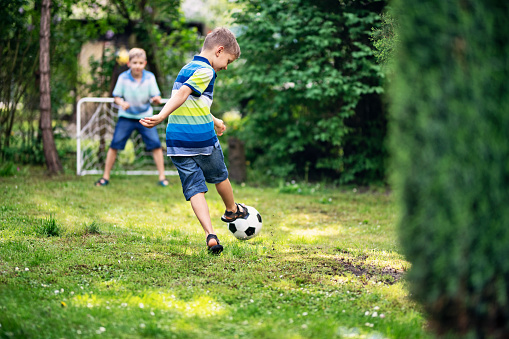 Little boys playing soccer in the garden. The boy is holding the ball and is laughing at the camera.\nNikon D850