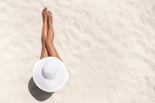 夏季節日時尚概念-曬黑婦女戴太陽帽子在海灘上從上面拍攝的白色沙子 - 腳 個照片及圖片檔