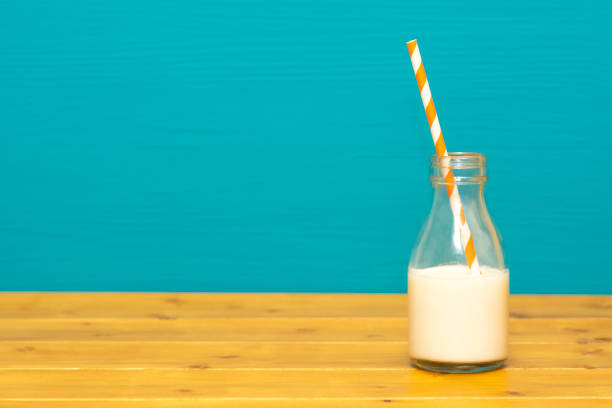 Glass milk bottle half full with a retro paper straw