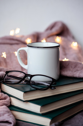 Still life details in home interior of living room. Sweaters and cup of tea on the books. Read, Rest. Cozy autumn or winter concept.