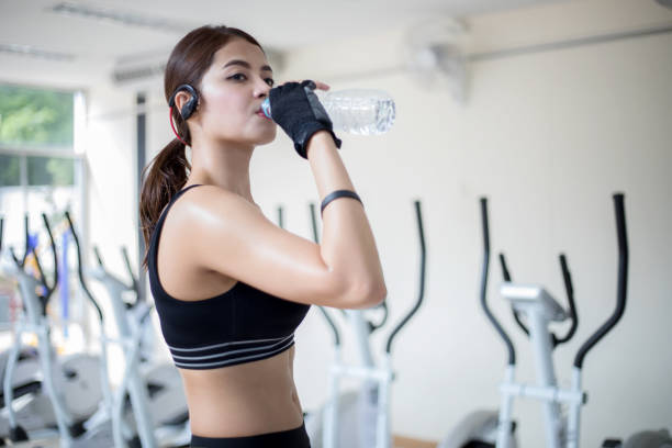 istock Young Woman Drinking Water While Standing At Gym 1128935378