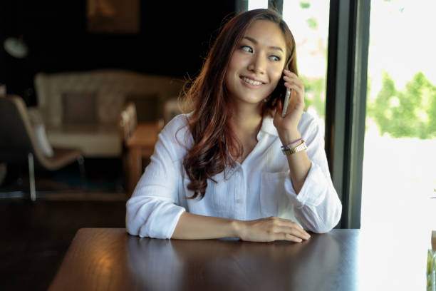istock Smiling Young Woman Talking On Mobile Phone While Sitting On Table 1128936239