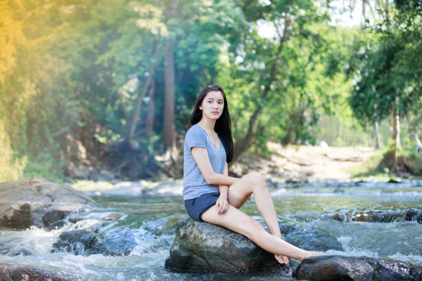 Fashionable beauty woman with curly hair in blue jeans with yellow top blouse and boots sits and rest on a vintage wooden pier near lake