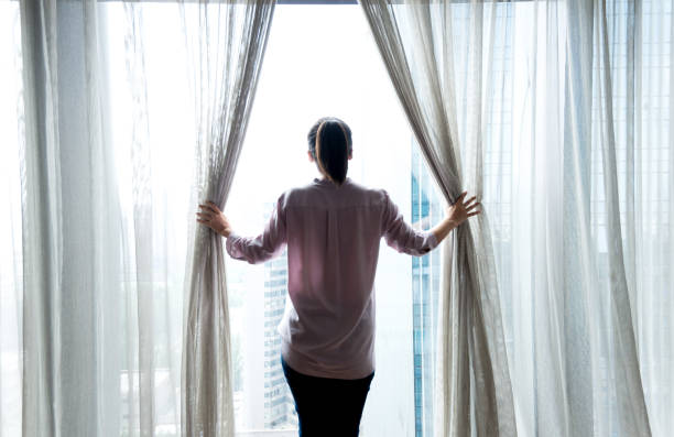 istock Woman opening curtains and looking out 1128937053