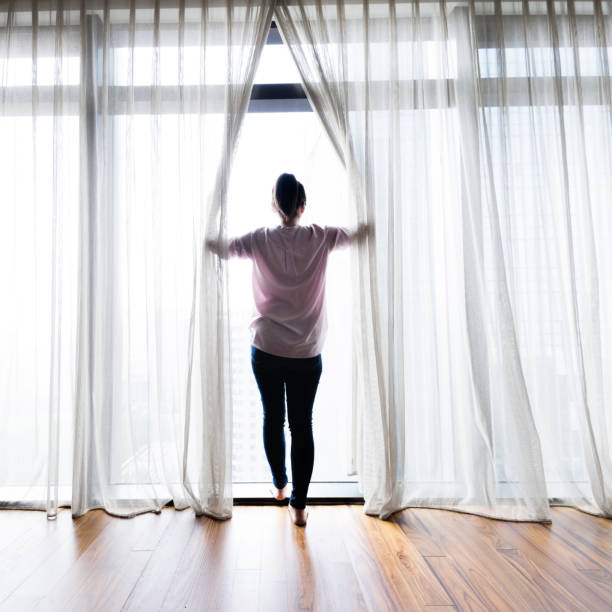 istock Woman opening curtains and looking out 1128937055
