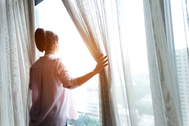 istock Woman opening curtains and looking out 1128937257