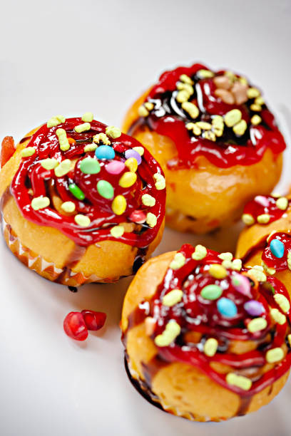 Close-up of garnished muffins with the toppings of sweet candy, jelly and dark chocolate syrup in white tray.