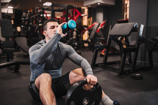 istock Muscular man drinking water while sitting on the floor in the gym. 1128944701