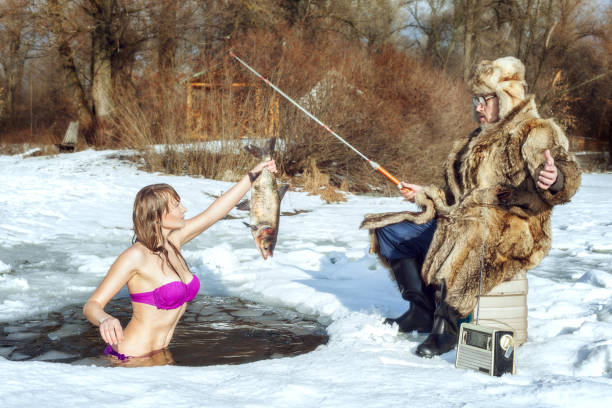 Young girl and elderly fisherman on winter fishing. Young girl in a swimsuit stands in the ice-hole and stretches the fish to an elderly fisherman. snow river stock pictures, royalty-free photos & images