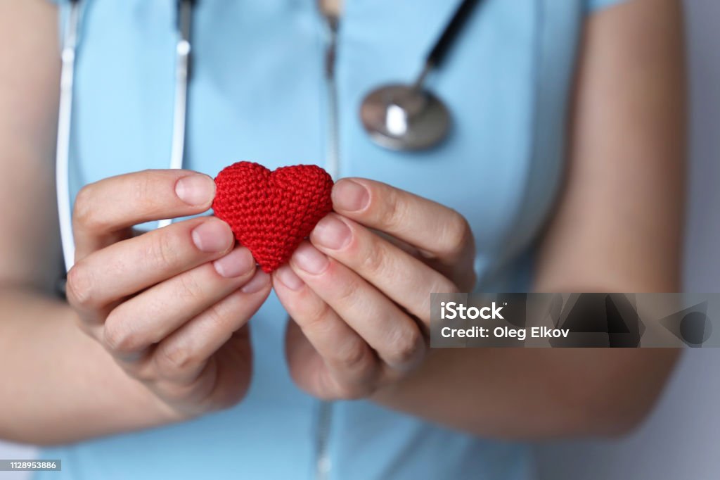 Health care, cardiology, woman doctor with stethoscope holding red knitted heart in hands Concept of blood donation, charity, treatment of heart disease in the clinic Celebration Stock Photo