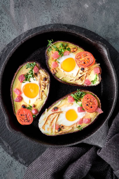 istock Keto diet dish: avocado boats with ham cubes, quail eggs, cheese and cherry tomatoes on iron cast skillet 1128955842