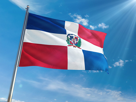 Dominican Republic National Flag Waving on pole against sunny blue sky background. High Definition