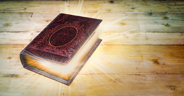 istock Antique book with magic lights on wooden background. 1128960112