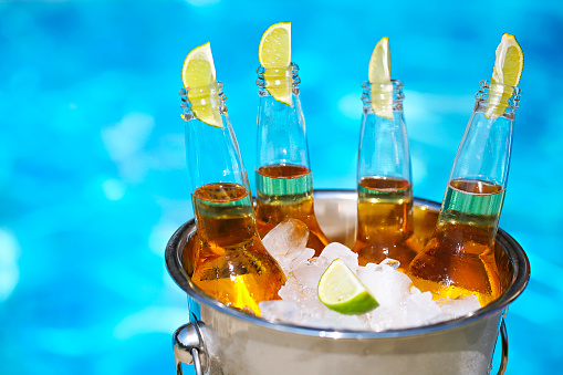 Closeup view of bucket with ice cubes, beer bottles and lime slices by the pool
