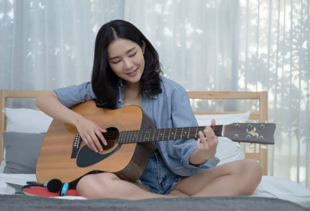 istock Young Asian woman playing guitar while staying in her bedroom. 1128963322