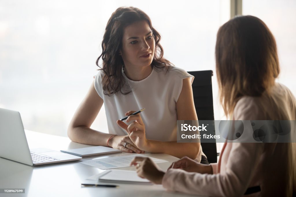 Two diverse serious businesswomen talking working together in office Two diverse serious businesswomen discussing business project working together in office, serious female advisor and client talking at meeting, focused executive colleagues brainstorm sharing ideas Discussion Stock Photo