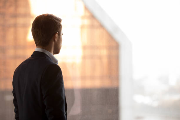 Rear view at rich businessman standing back looking at window