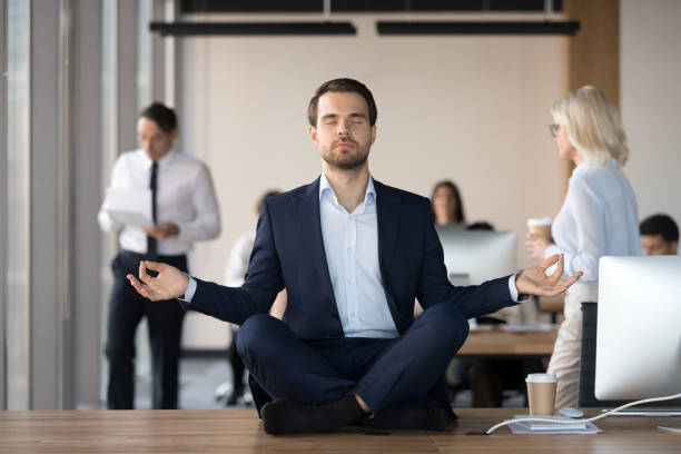 事務所の仕事の机の上で瞑想のスーツで穏やかなビジネスマン - zen like meditating yoga business ストックフォトと画像