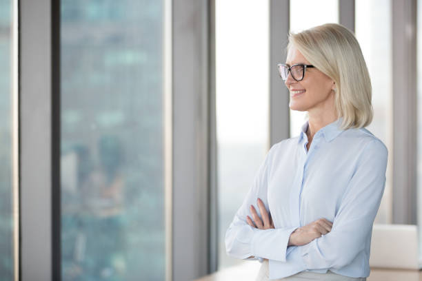 istock Smiling successful middle aged businesswoman looking through window 1128967674