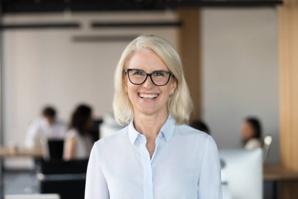 cheerful senior businesswoman in glasses looking at camera in office - women professor mature adult human face imagens e fotografias de stock