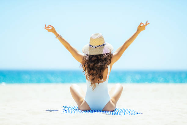 istock woman on ocean coast rejoicing while sitting on striped towel 1128969371