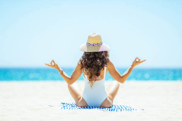 istock woman doing yoga while sitting on striped towel on seashore 1128969416