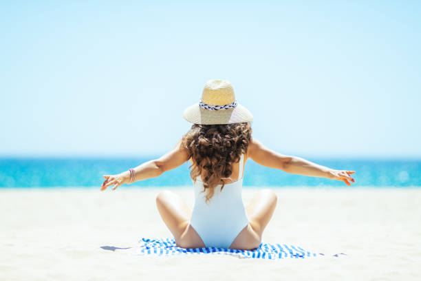 istock woman rejoicing while sitting on striped towel on seacoast 1128969455