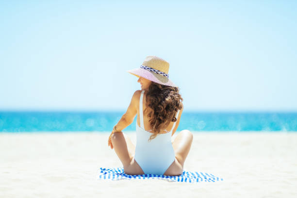 istock woman looking aside while sitting on striped towel on beach 1128969470