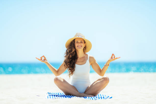 istock woman doing yoga while sitting on striped towel on seashore 1128969599