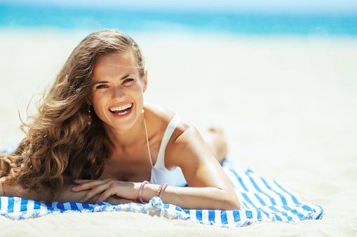 Portrait of happy young woman in white swimwear laying on a striped towel on the seacoast. quiet vacation heaven. Hair healthy condition. minimal to no crowd peace. total relaxation on the best beach