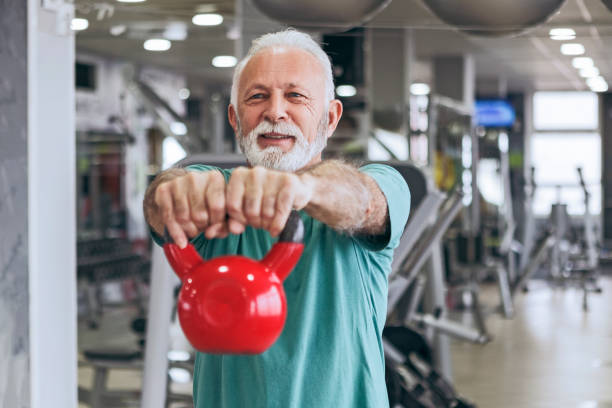 Senior man in gym using kettle bells Senior man in gym working out using kettle bells kettlebell stock pictures, royalty-free photos & images