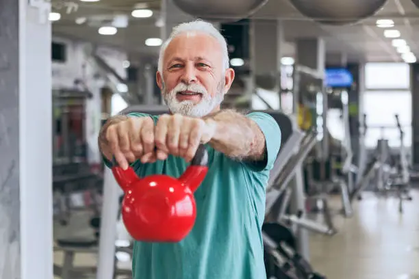 Photo of Senior man in gym using kettle bells