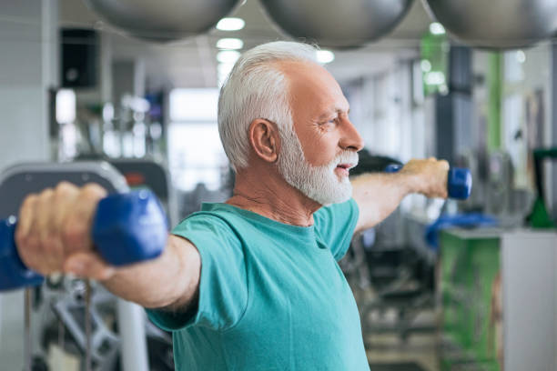 istock Senior man holding barbells with outstretched arms 1128969808