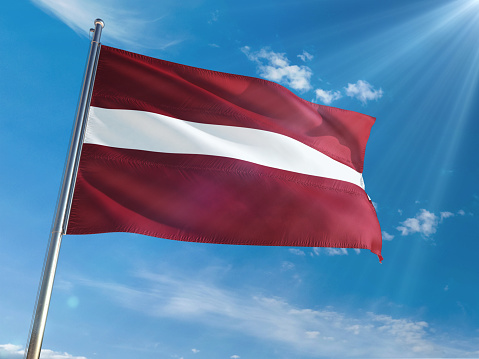 Latvia National Flag Waving on pole against sunny blue sky background. High Definition
