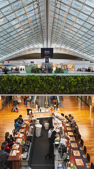 CDG Paris Airport - 12/22/18: Terminal 2F food court, huge skylight mesh with live vegetation, vertical garden and a bar. People travelling with suitcases