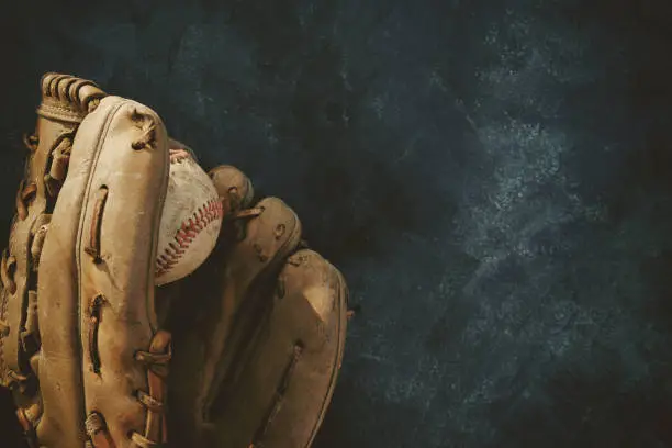 Old vintage ball in baseball glove flat lay shows close up of sports equipment with black background.